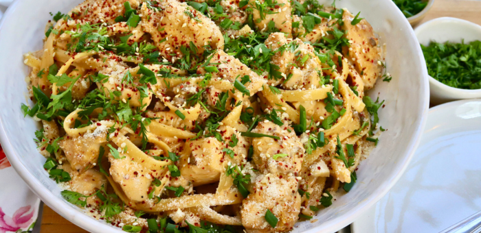 Warm bowl of sautéed chicken breast tossed with fettuccine noodles, white miso sauce, and kimchi, garnished with parsley, sesame seeds, and red pepper flakes.