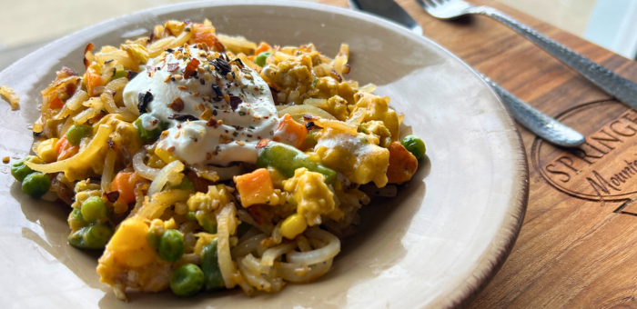 Loaded ground chicken hashbrowns with vegetables, melted cheese, and a creamy topping served on a plate.