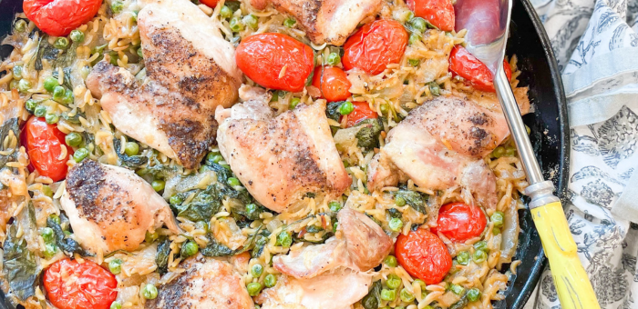 One-pot chicken orzo bake with tomatoes, peas, and spinach in a skillet.