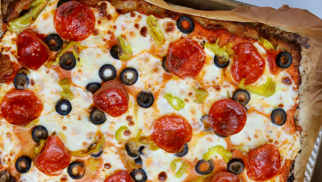 High-protein pizza made with a ground chicken crust, topped with melted mozzarella, pepperoni, black olives, banana peppers, and marinara sauce.