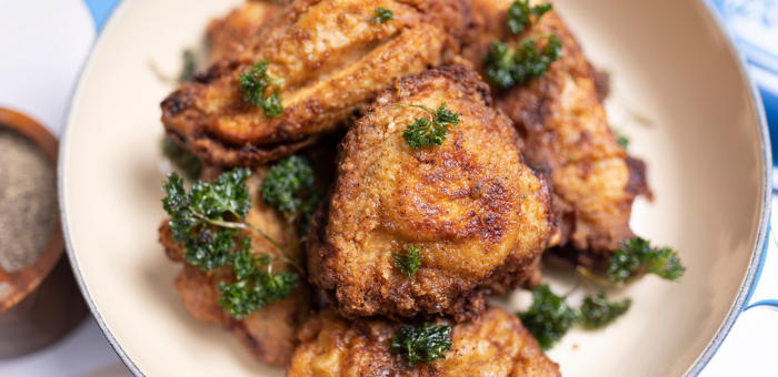 Golden brown Southern fried chicken thighs garnished with fresh parsley, served in a white bowl for a classic comfort food presentation.