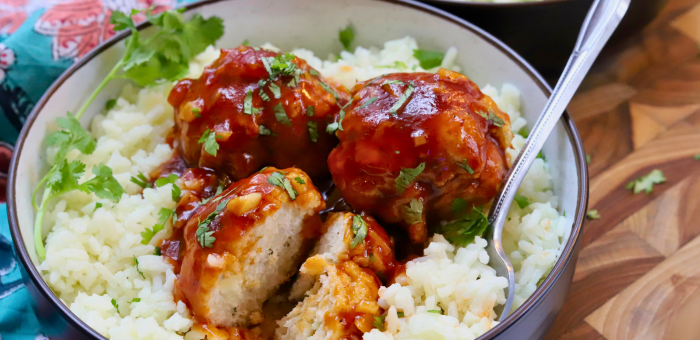 Sticky sweet and sour ground chicken meatballs served over rice and garnished with fresh herbs.