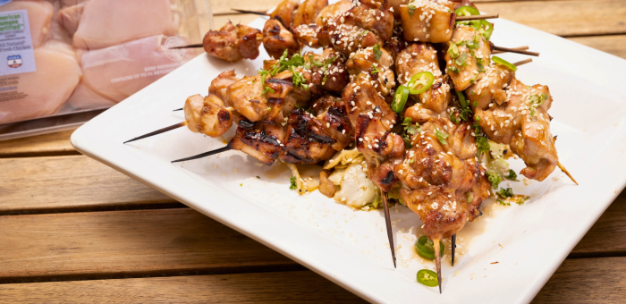 Grilled chicken yakitori skewers glazed with soy-based sauce, garnished with sesame seeds and sliced green chili, served on a white plate with Springer Mountain Farms chicken packaging in the background.