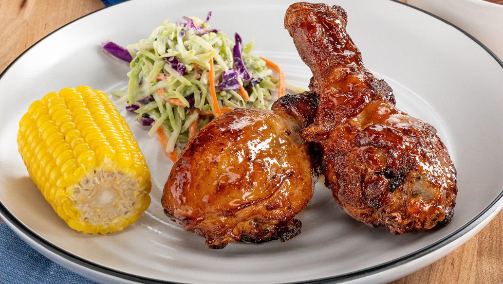 Air fryer chicken drumsticks glazed with peach BBQ sauce served with coleslaw and corn on the cob