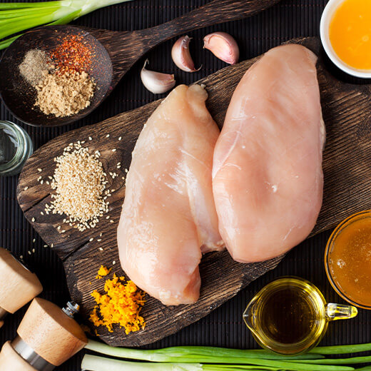 raw chicken breast shown on preparation board with other spices