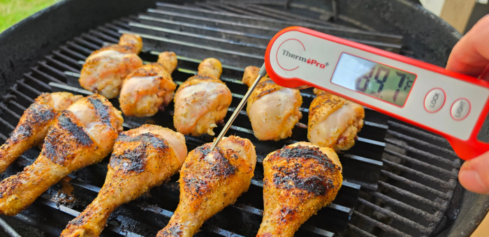 checking internal temperature of grilled chicken drumsticks with thermometer