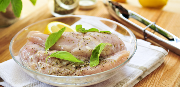 chicken breasts in a citrus herb marinade in glass bowl on a towel and cutting board with tongs and other ingredients