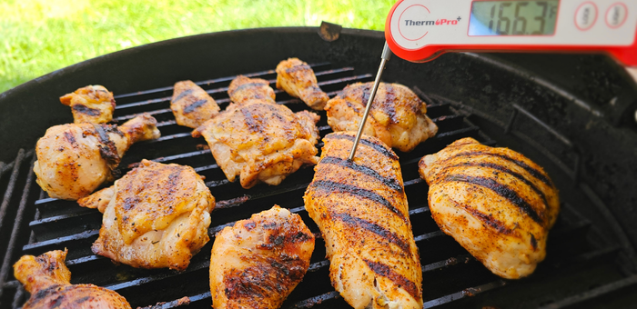 grilled chicken breasts thighs wings and drumsticks on a barbecue grill with thermometer showing 165 degrees