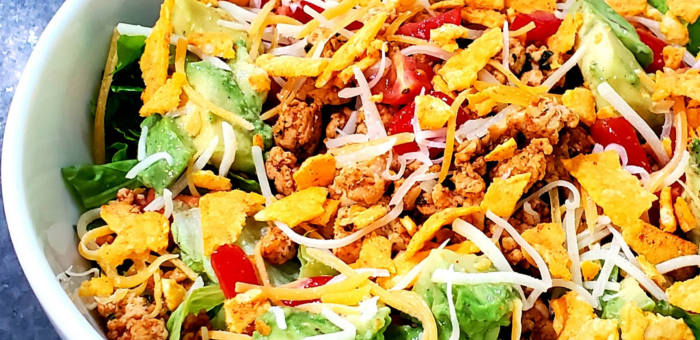 Ground chicken taco salad with avocado, shredded cheese, tortilla strips, and fresh vegetables for a quick and easy weeknight dinner.