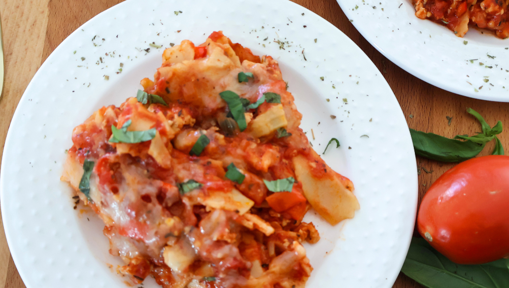 Lazy lasagna made with ground chicken, lasagna noodles, tomato sauce, and melted mozzarella topped with fresh basil on a white plate.