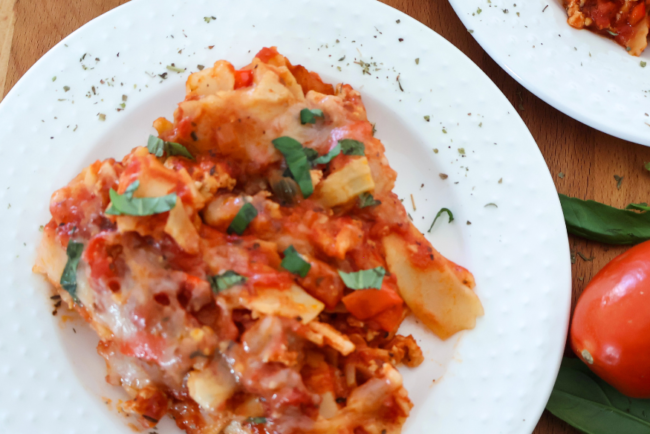 Lazy lasagna made with ground chicken, lasagna noodles, tomato sauce, and melted mozzarella topped with fresh basil on a white plate.