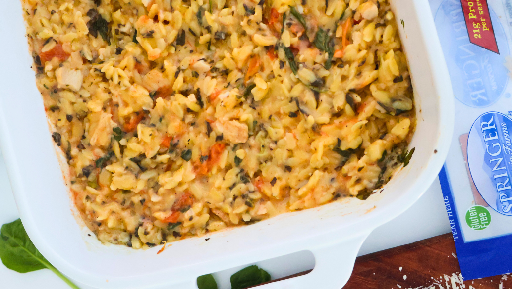 One pan spinach artichoke chicken orzo bake in a white casserole dish with roasted chicken, tomatoes, and spinach