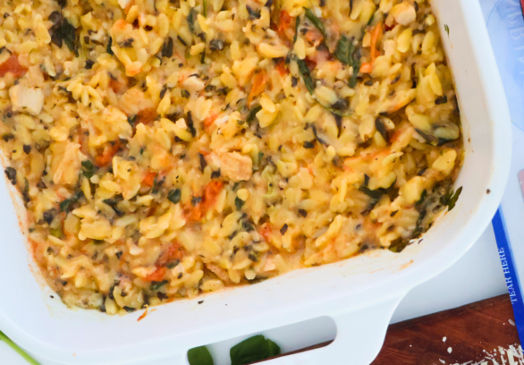 One pan spinach artichoke chicken orzo bake in a white casserole dish with roasted chicken, tomatoes, and spinach