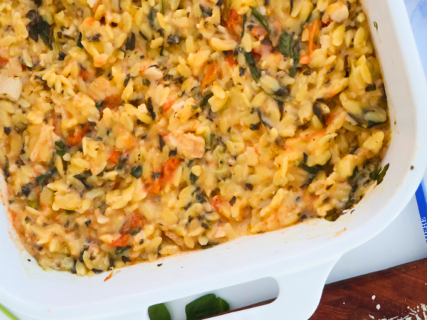One pan spinach artichoke chicken orzo bake in a white casserole dish with roasted chicken, tomatoes, and spinach