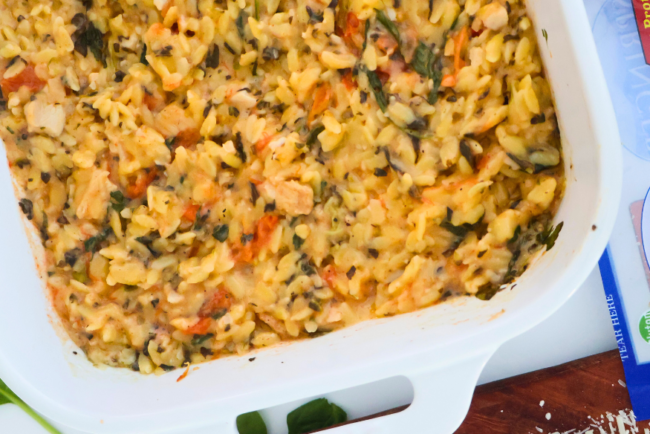 One pan spinach artichoke chicken orzo bake in a white casserole dish with roasted chicken, tomatoes, and spinach