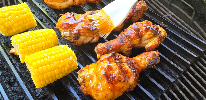 brushing sauce on fully cooked chicken drumsticks on grill