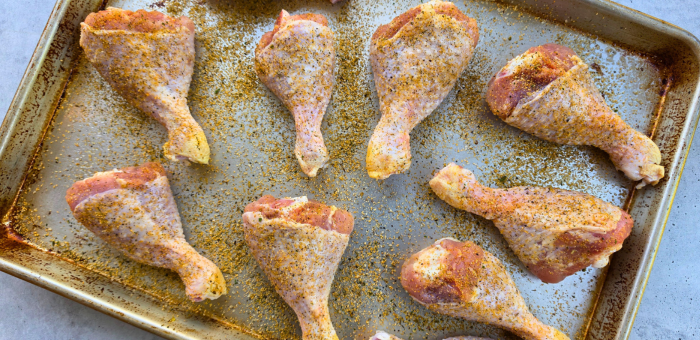 raw chicken drumsticks seasoned on sheet pan before grilling