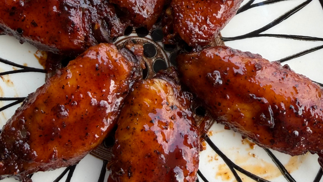 Close-up of smoky barbecue chicken wings coated in a thick, glossy BBQ sauce, arranged on a decorative plate with a rich caramelized finish and charred edges.