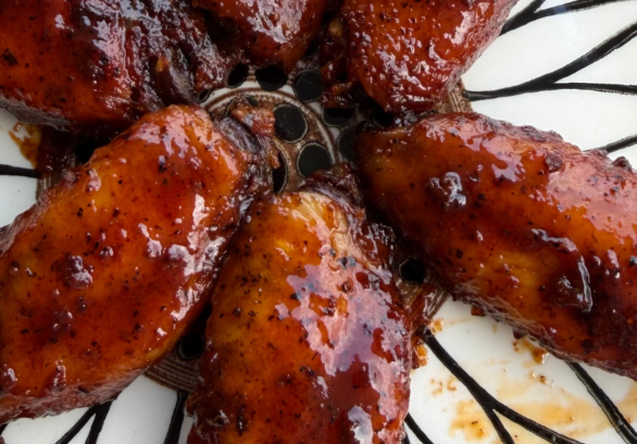 Close-up of smoky barbecue chicken wings coated in a thick, glossy BBQ sauce, arranged on a decorative plate with a rich caramelized finish and charred edges.