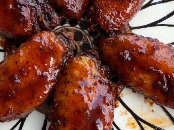 Close-up of smoky barbecue chicken wings coated in a thick, glossy BBQ sauce, arranged on a decorative plate with a rich caramelized finish and charred edges.