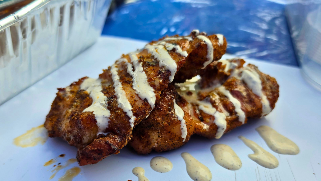 Smoked boneless skinless chicken thighs drizzled with Alabama white sauce on a serving tray, featuring crispy bark and smoky grilled flavor.