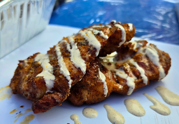 Smoked boneless skinless chicken thighs drizzled with Alabama white sauce on a serving tray, featuring crispy bark and smoky grilled flavor.