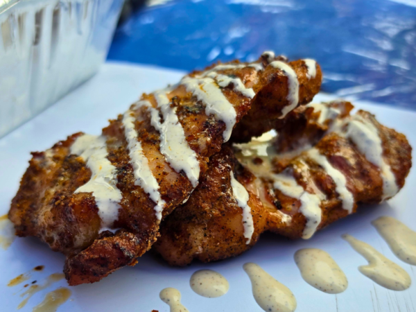 Smoked boneless skinless chicken thighs drizzled with Alabama white sauce on a serving tray, featuring crispy bark and smoky grilled flavor.