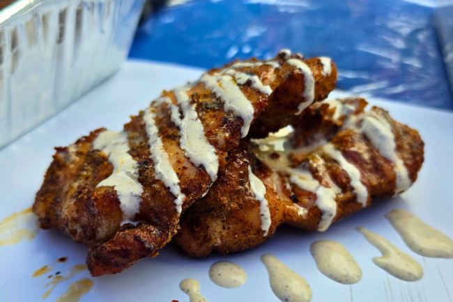 Smoked boneless skinless chicken thighs drizzled with Alabama white sauce on a serving tray, featuring crispy bark and smoky grilled flavor.